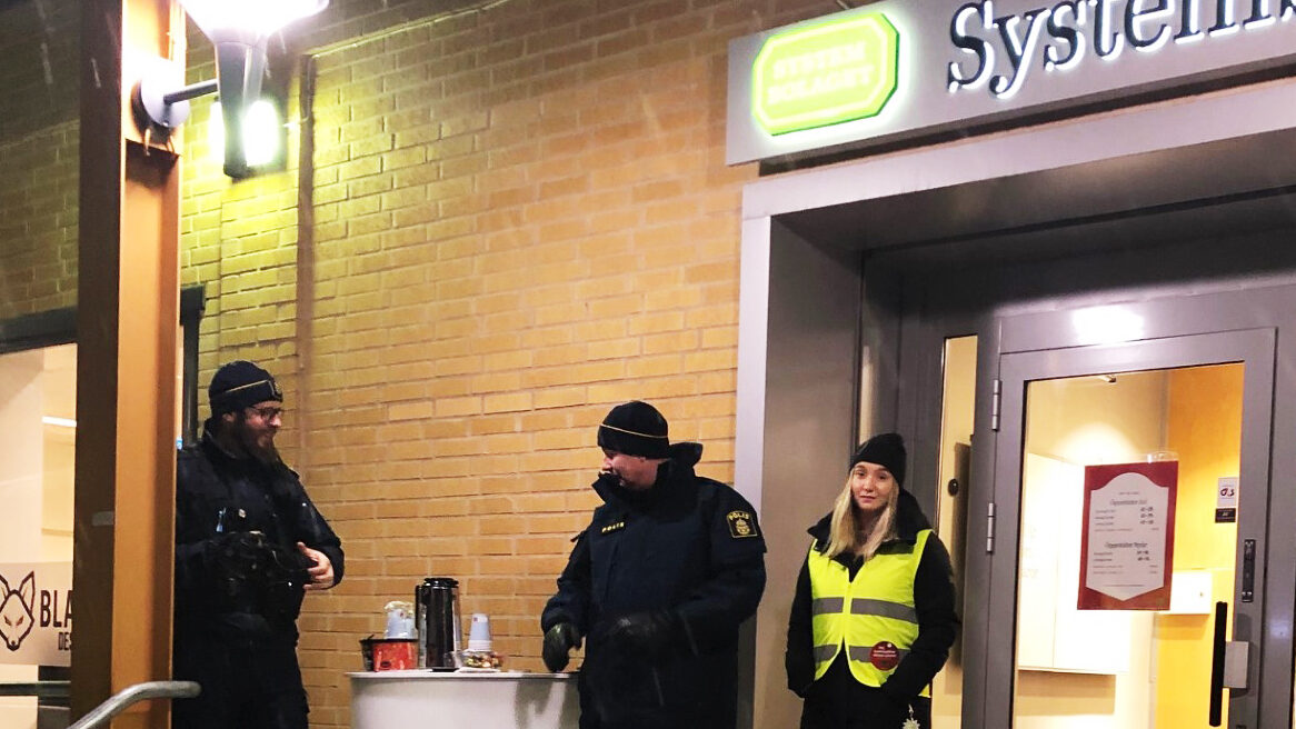 Vit jul 2023 Två poliser och en representant för Kvinnojouren står utanför Systembolaget i Övertorneå. Det snöar och är mörkt ute. De ser glada ut.